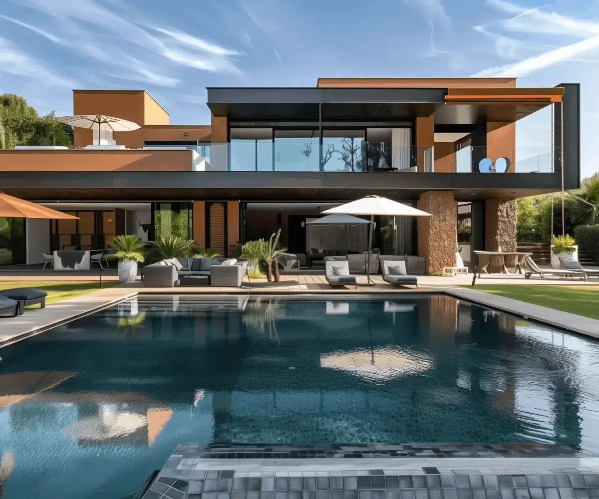 Modern luxury villa with a pool, sun loungers, parasols, and a lush green garden.