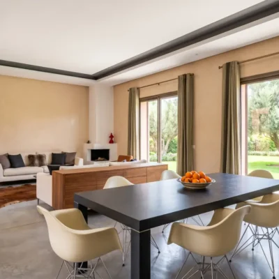 Open-plan villa dining and living room with dark table, Eames chairs, fireplace and olive garden view