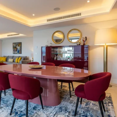 Elegant dining room with oval pink lacquered table, burgundy velvet chairs and twin gold circular mirrors