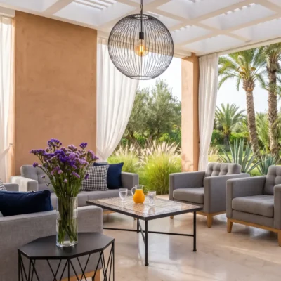 Covered villa terrace with grey armchairs, mosaic coffee table, white curtains and palm garden pool view