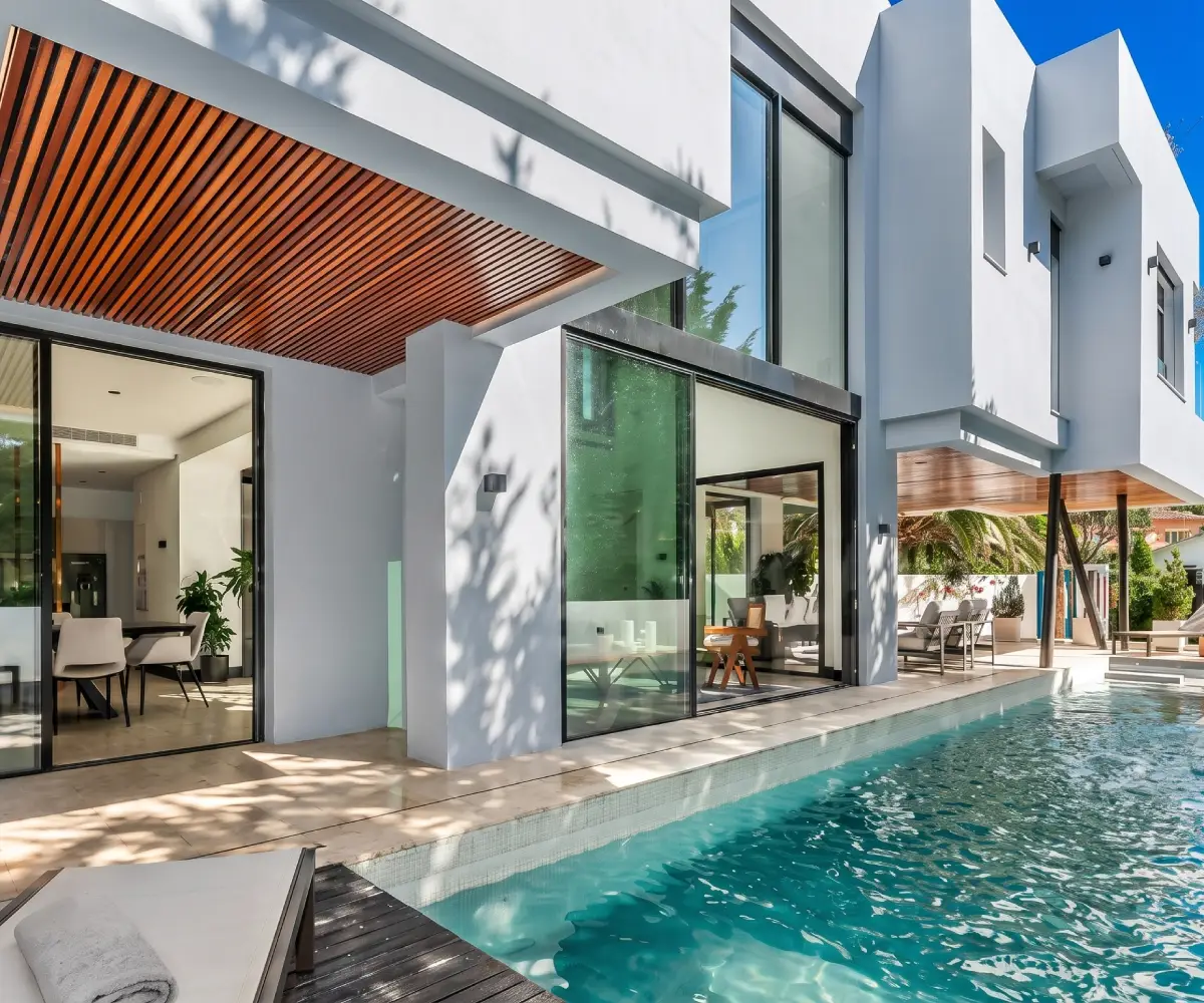 Contemporary villa exterior with lap pool, wood slat pergola and glass sliding doors under blue sky