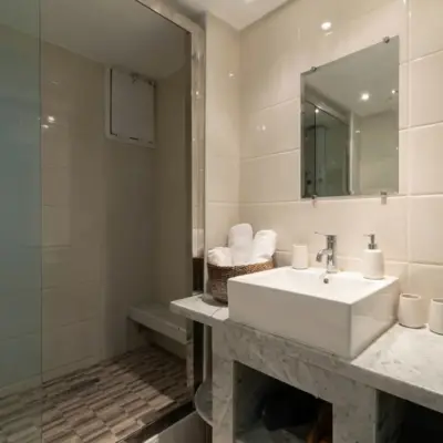 Bathroom with walk-in shower, white Carrara marble vanity, vessel washbasin, wall mirror and basket of rolled towels