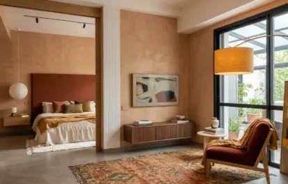 Artist loft and studio for rent in Asilah with a living area, rust armchair, Moroccan rug and a bedroom alcove beyond