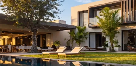 Buying a luxury villa in Morocco – Modern two-storey facade with pool, sun loungers and tropical garden at golden hour